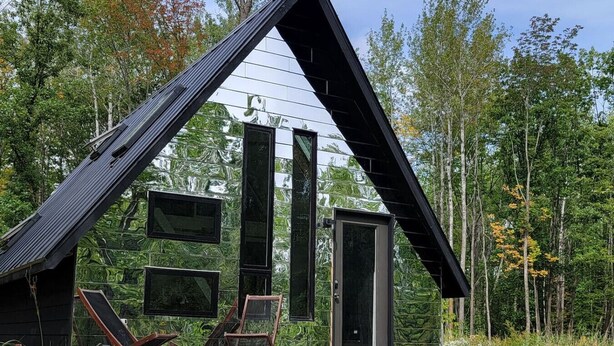 Een moderne houten hut met een puntig dak, grote ramen en een deur.