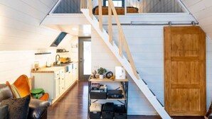 Een loft-achtige woonruimte met een houten trap, een bank, een salontafel en een keukenhoek.