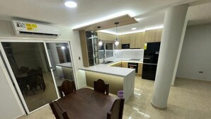 Une cuisine moderne dotée d’un îlot central, d’un coin repas avec une table et des chaises, et d’une porte-fenêtre coulissante donnant sur un espace extérieur.