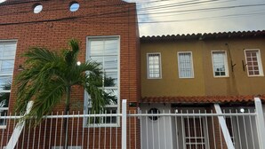 Un immeuble résidentiel avec une façade en briques, un portail blanc et un palmier.
