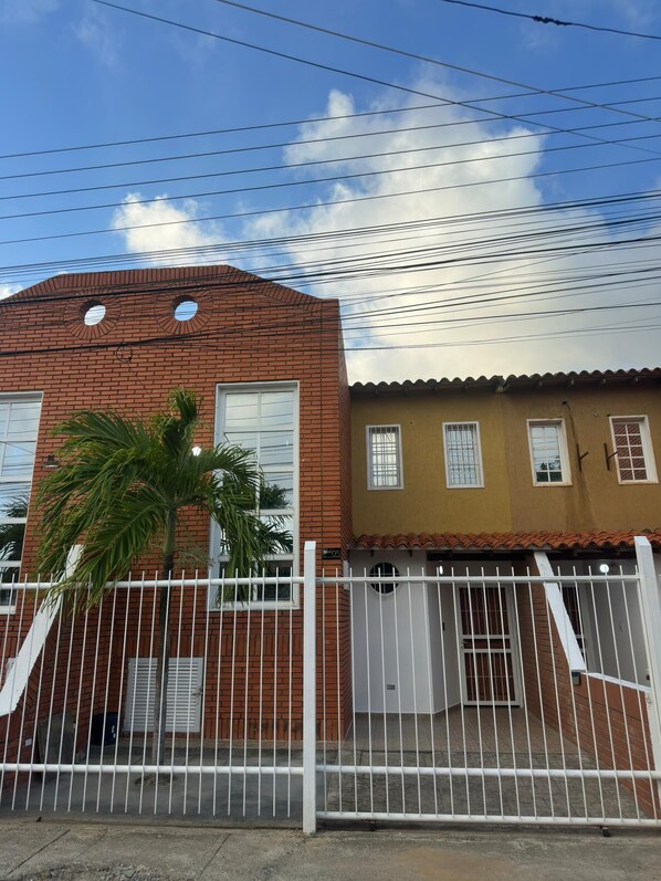 A residential building with a brick facade, a white gate, and a palm tree.