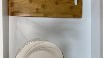 Un cajón blanco con una tabla de cortar de madera y una pila de platos blancos.