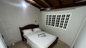 Une chambre avec un lit en bois, du linge de lit blanc, une fenêtre à carreaux et un sol carrelé.