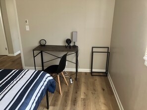 A room with a bed, a desk with a chair, a standing fan, and a power outlet.