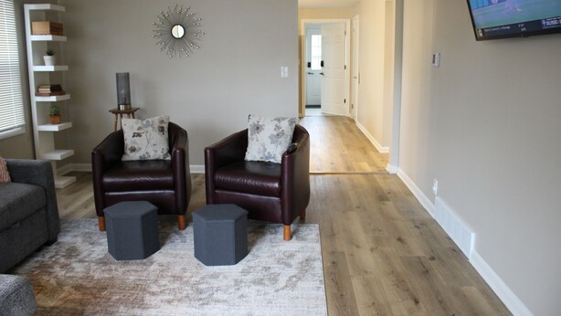Una sala de estar con dos sillones de cuero, un sofá gris, una mesita auxiliar y un espejo decorativo en la pared.