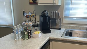 Una cocina equipada con lavavajillas, cafetera, botellas de agua y un portal cápsulas de café.