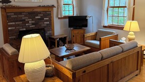A living room with a fireplace, wooden furniture, a television, and windows with curtains.