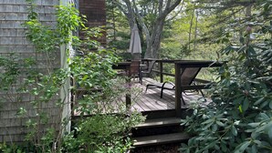 A wooden deck with outdoor furniture, a brick wall, and a view of trees.