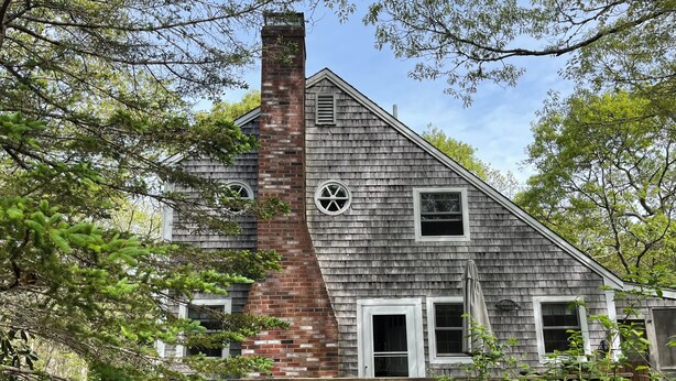 A two-story house with a brick chimney, a wooden deck, and a wooden fence.