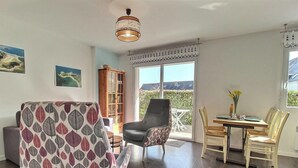Ein Zimmer mit Esstisch, Stühlen, einer Couch, einem Bücherregal und einem großen Fenster mit Blick.