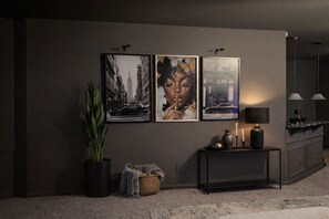 Een moderne woonkamer met een donkergrijze bank, een bijzettafeltje met een lamp, een kamerplant en twee ingelijste kunstwerken aan de muur.