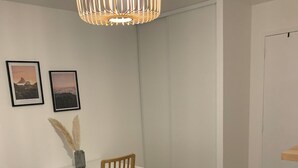 Ein Zimmer mit einem weißen Schreibtisch, einem Holzstuhl, einer Pendelleuchte und zwei gerahmten Bildern an der Wand.