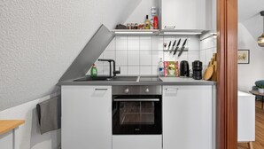 Eine moderne Küche mit weißen Schränken, einem Backofen, einer Spüle und einer Arbeitsplatte mit verschiedenen Küchenutensilien.