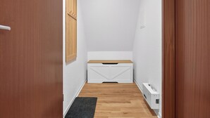 Ein schmaler Korridor mit einer Holztür, einer weißen Bank und einer weißen Wand.
