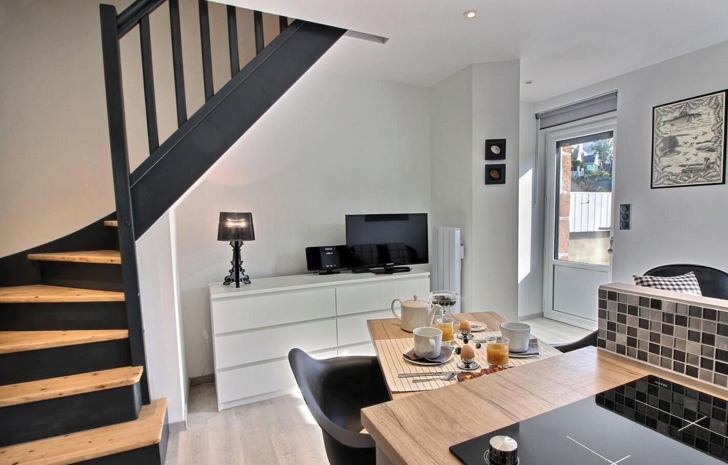A modern kitchen with a dining table, chairs, a TV, and a staircase.