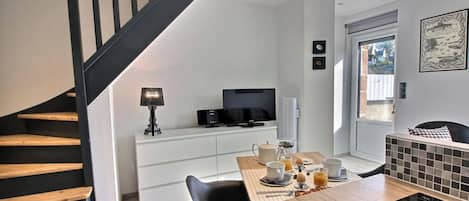 A modern kitchen with a dining table, chairs, a TV, and a staircase.
