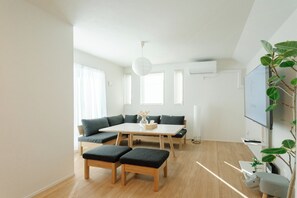 A modern living room with a sofa, a dining table, and a TV mounted on the wall.