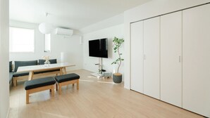 Een moderne woonkamer met een flatscreen televisie, een eettafel, banken, een potplant en een garderobe.