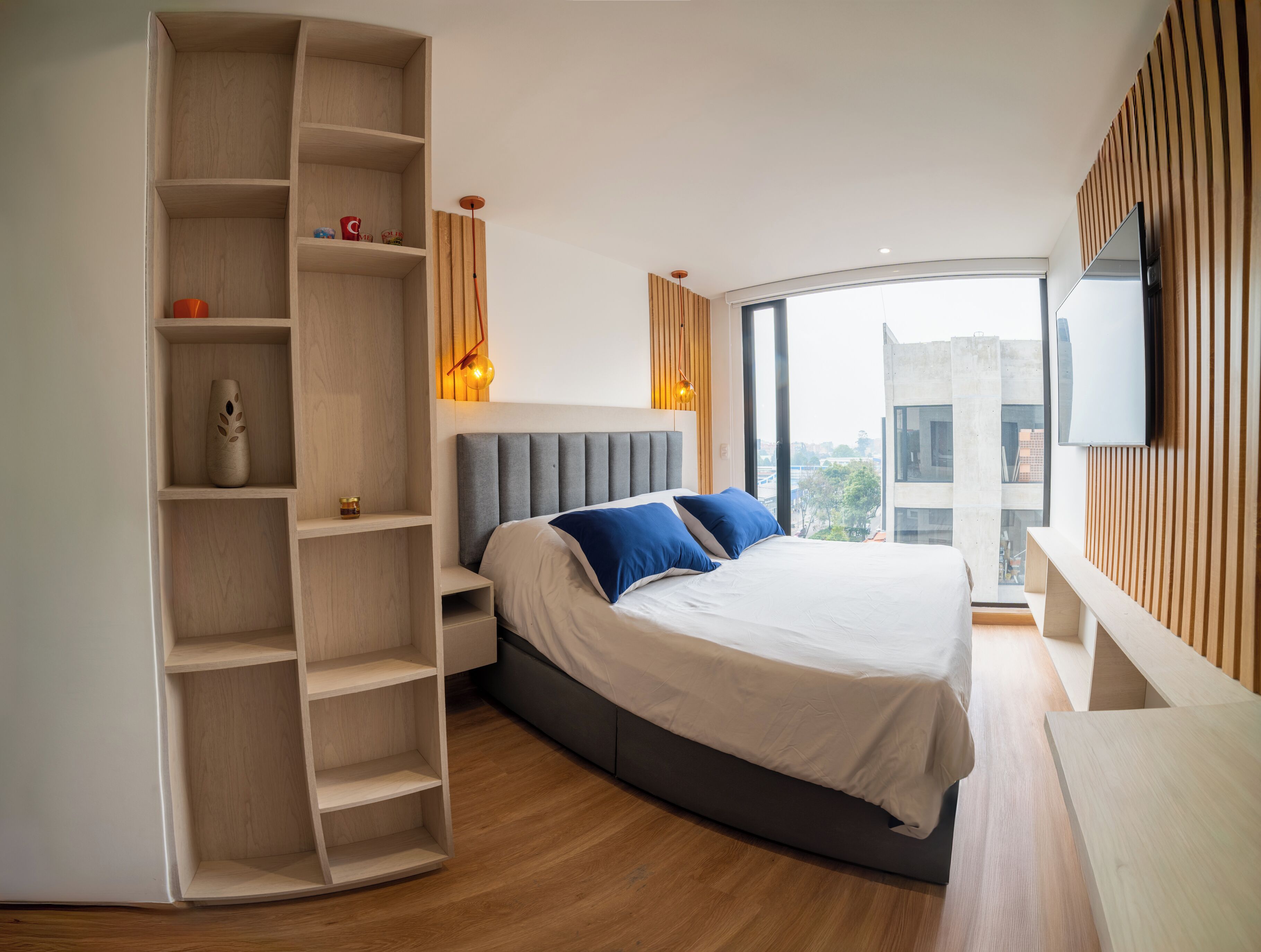 Un dormitorio moderno con una cama grande, estanterías empotradas, televisión y vista a la ciudad.