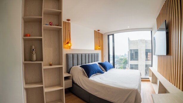 Un dormitorio moderno con una cama grande, estanterías empotradas, televisión y vista a la ciudad.