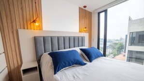 Un dormitorio moderno con una cama grande, mesitas de noche integradas y vistas a la ciudad.