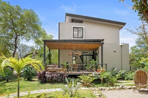A modern house with a covered patio, surrounded by lush greenery.