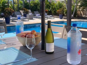 Ein Tisch am Pool mit einer Weinflasche, einer Obstschale und einer Flasche Fiji-Wasser.