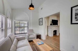 Ein Wohnzimmer mit einer Couch, einem Sessel, einem Couchtisch, einem Kamin und einem Fernseher.