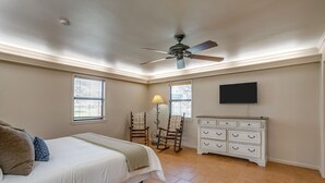 Ein Schlafzimmer mit einem Bett, einem Schminktisch, zwei Schaukelstühlen, einem Deckenventilator und einem an der Wand befestigten Fernseher.
