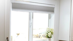 Une cuisine avec un plan de travail blanc, un robinet noir, une fenêtre avec des stores et un vase de fleurs posé sur le rebord de la fenêtre.