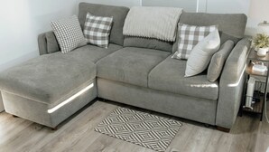 Un canapé d’angle gris, agrémenté d’un plaid blanc, de coussins à carreaux et d’un tapis à motifs géométriques.