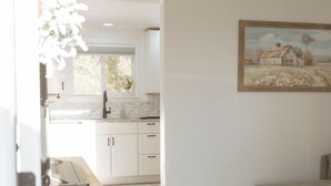 Une cuisine moderne avec des meubles blancs, un coin repas avec une table et un tableau accroché au mur.