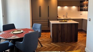A modern kitchen with a central island, wooden cabinets, and a dining area with a red tablecloth. - 2-bedroom apartment in lovely London with air conditioning (London)