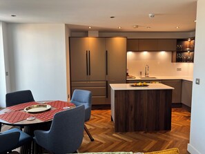 Una cuina moderna amb una illa central, armaris de fusta i una zona de menjador amb estovatge vermell.