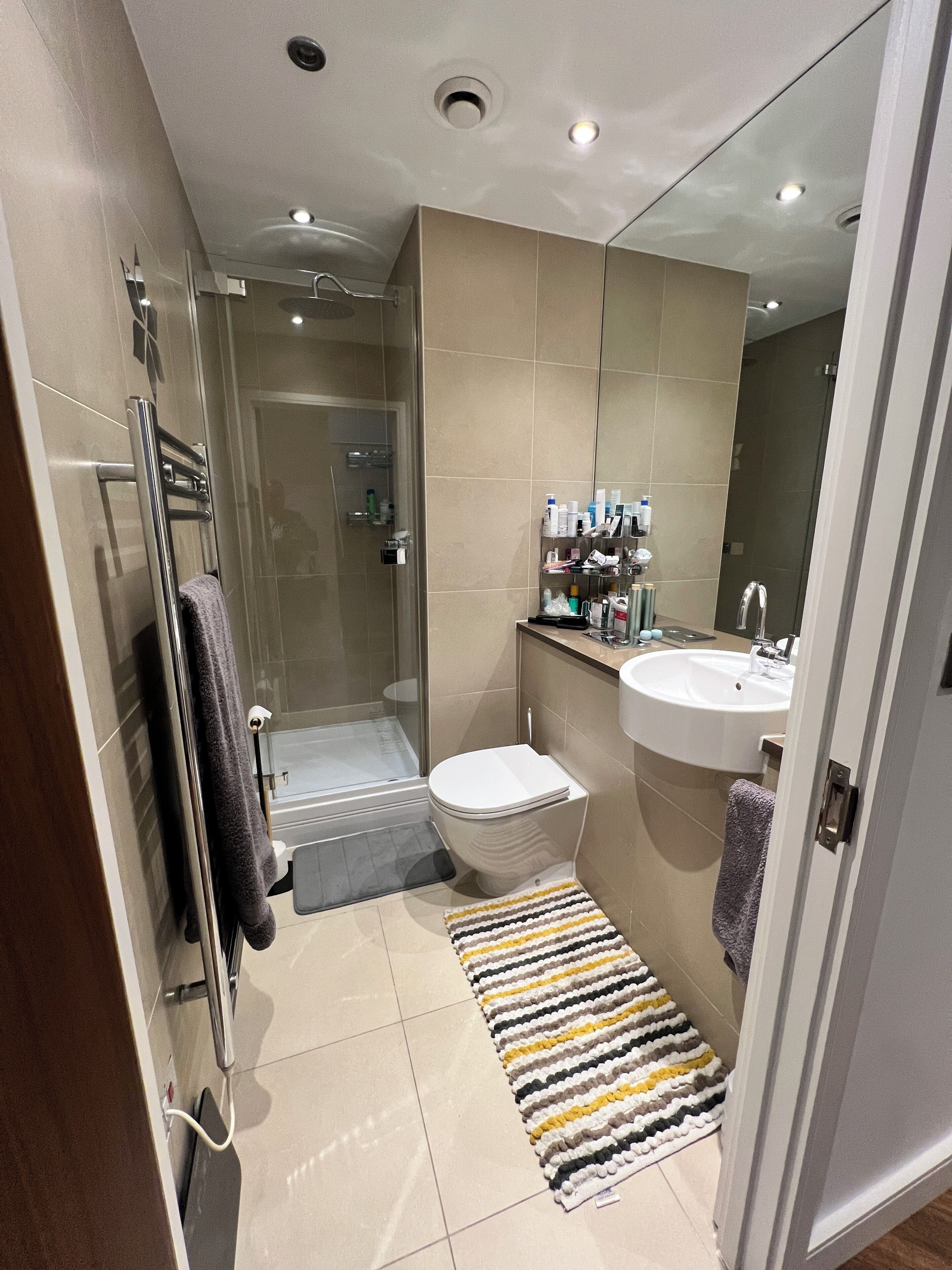 A modern bathroom with a glass shower enclosure, a toilet, a sink, and a towel rack.