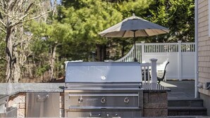 An outdoor grill with a control panel, a stone base, and a white fence in the background. - Hoppy Place: 066-M Expansive Deck area, Hot Tub, Walk to Salt Water (Mashpee)
