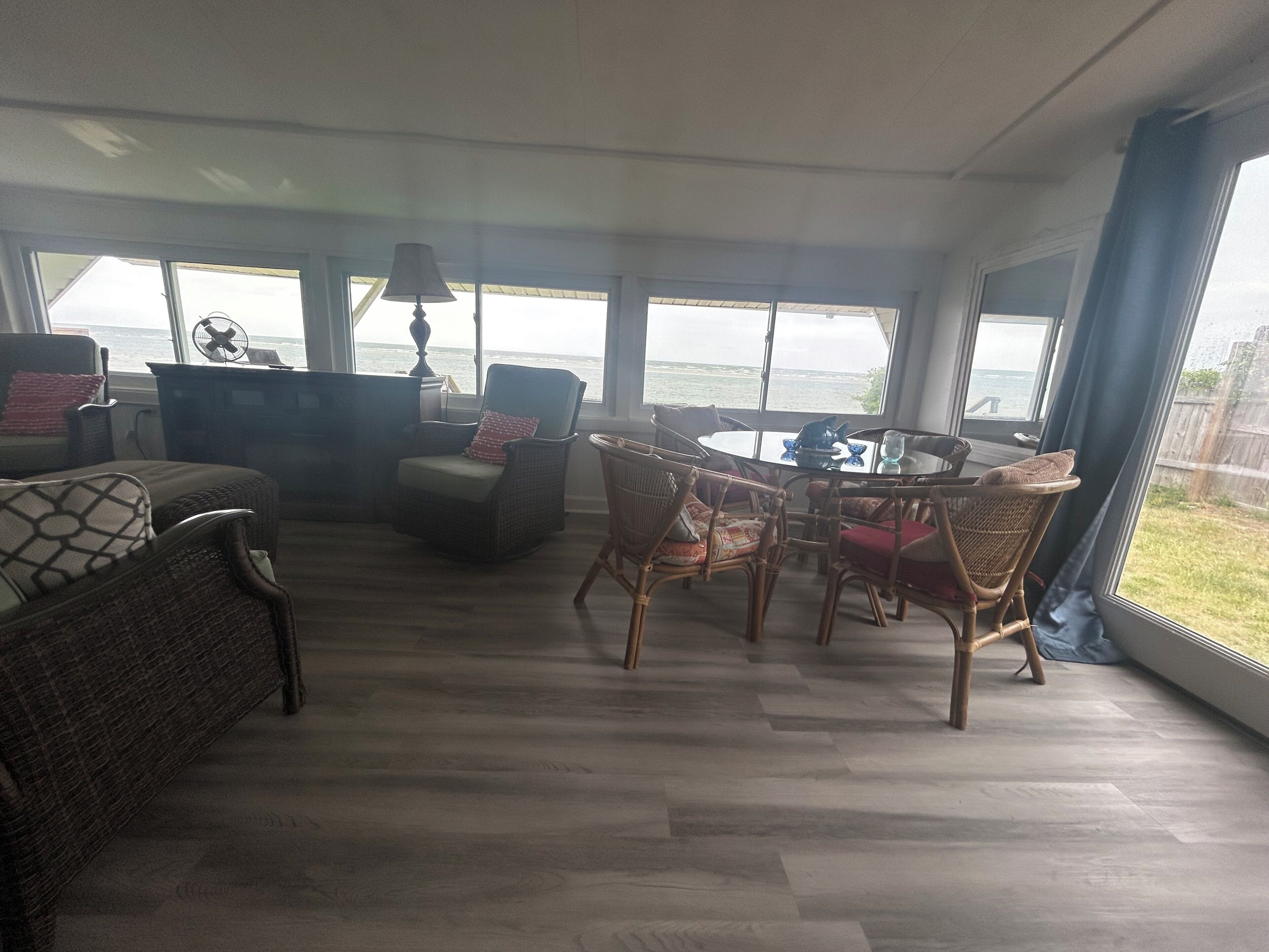 A spacious living area with a view of the ocean, wicker furniture, and a dining table.