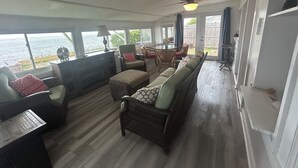 A spacious room with a large window overlooking the sea, a ceiling fan, and a dining area with chairs and a table. - Smith Beach cottage w/ private sunset (Cape Charles)