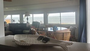 A room with a view of the sea, a table with a fish-shaped tray, wicker furniture, and a lamp. - Smith Beach cottage w/ private sunset (Cape Charles)