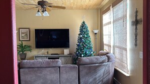 Un salon avec une télévision, un sapin de Noël et un ventilateur de plafond.