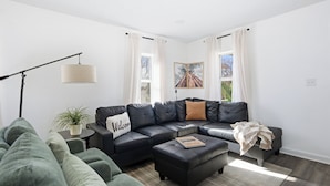 A modern living room with a sectional sofa, a black leather couch, a coffee table, and a floor lamp. - Family Arcade Home Pets OK Near Red Rocks (Englewood)