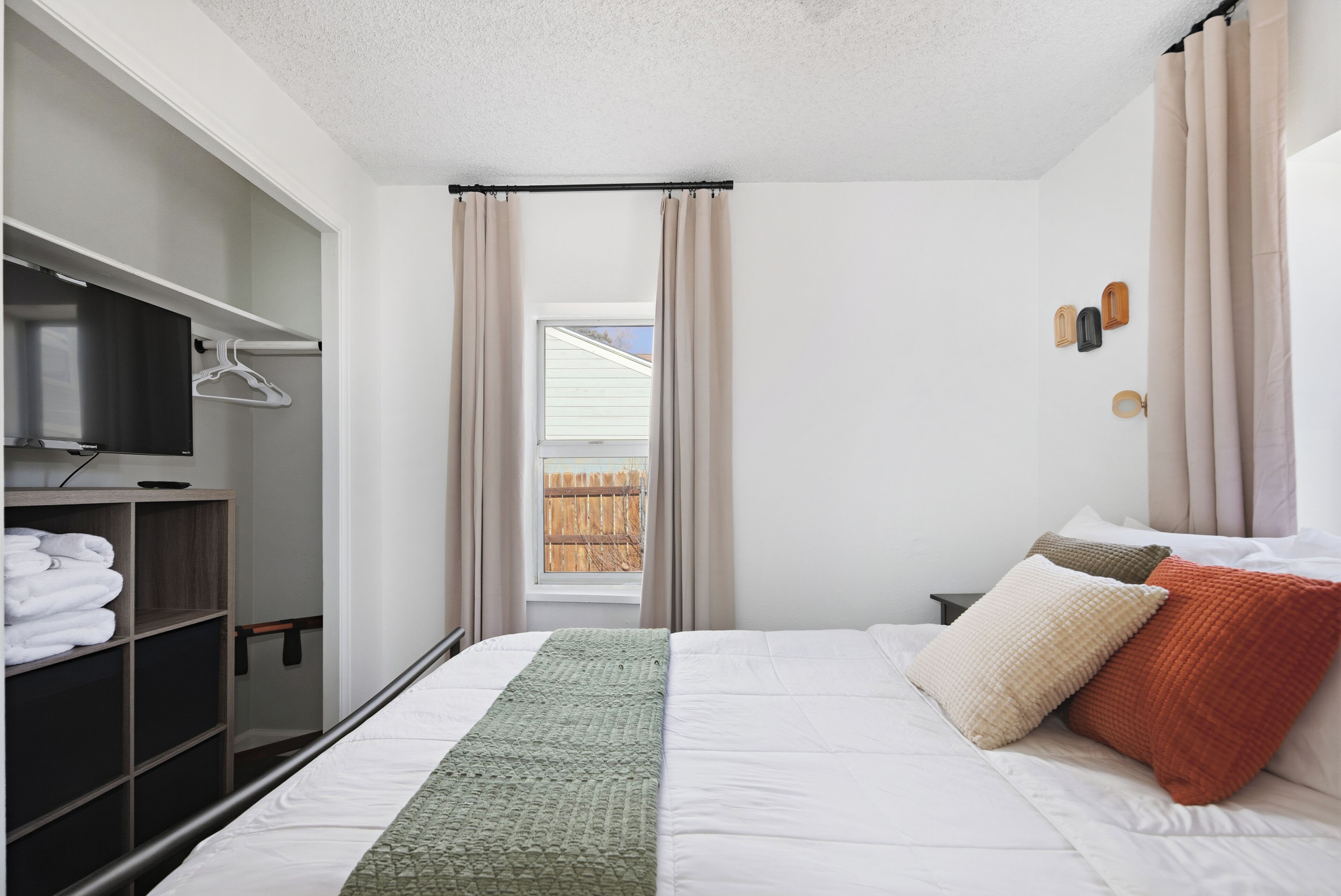Un dormitorio con cama, televisión, armario y ventana con cortinas.