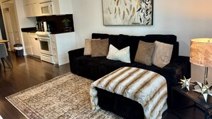 A modern living room with a black sofa, a patterned rug, and a dining area with white cabinetry and a microwave.