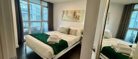 Une chambre d’hôtel moderne avec un grand lit, une vue sur la ville grâce à de grandes fenêtres du sol au plafond et un tableau accroché au mur.