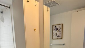 A modern bathroom with a white sink, mirror, and toilet. There is a towel on the sink, a potted plant, and a framed artwork on the wall.