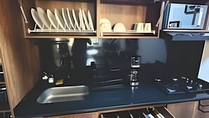 A compact kitchen with wooden cabinets, a black countertop, and a built-in stove. - Epic Suite 313 Family Airport 3Room10Pax (Pereira)