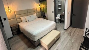 A modern bedroom with a bed, bedside tables, a bench, an air conditioning unit, and a bathroom visible through an open door. - Epic Suite 313 Family Airport 3Room10Pax (Pereira)
