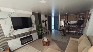 A modern living room with a flat-screen TV, a fireplace, a sofa, and a dining area with bar stools. - Epic Suite 313 Family Airport 3Room10Pax (Pereira)