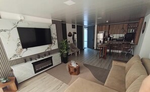 A modern living room with a flat-screen TV, a fireplace, a sofa, and a dining area with bar stools. - Epic Suite 313 Family Airport 3Room10Pax (Pereira)