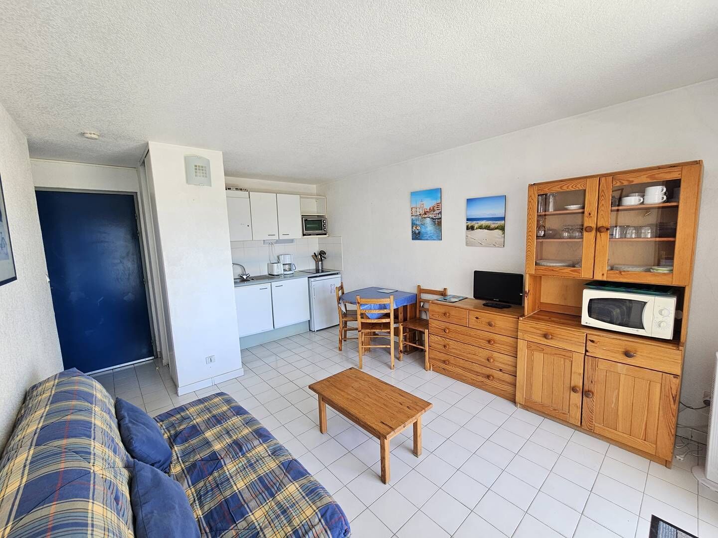 A compact living space with a kitchenette, a dining area, a sofa, and a television.